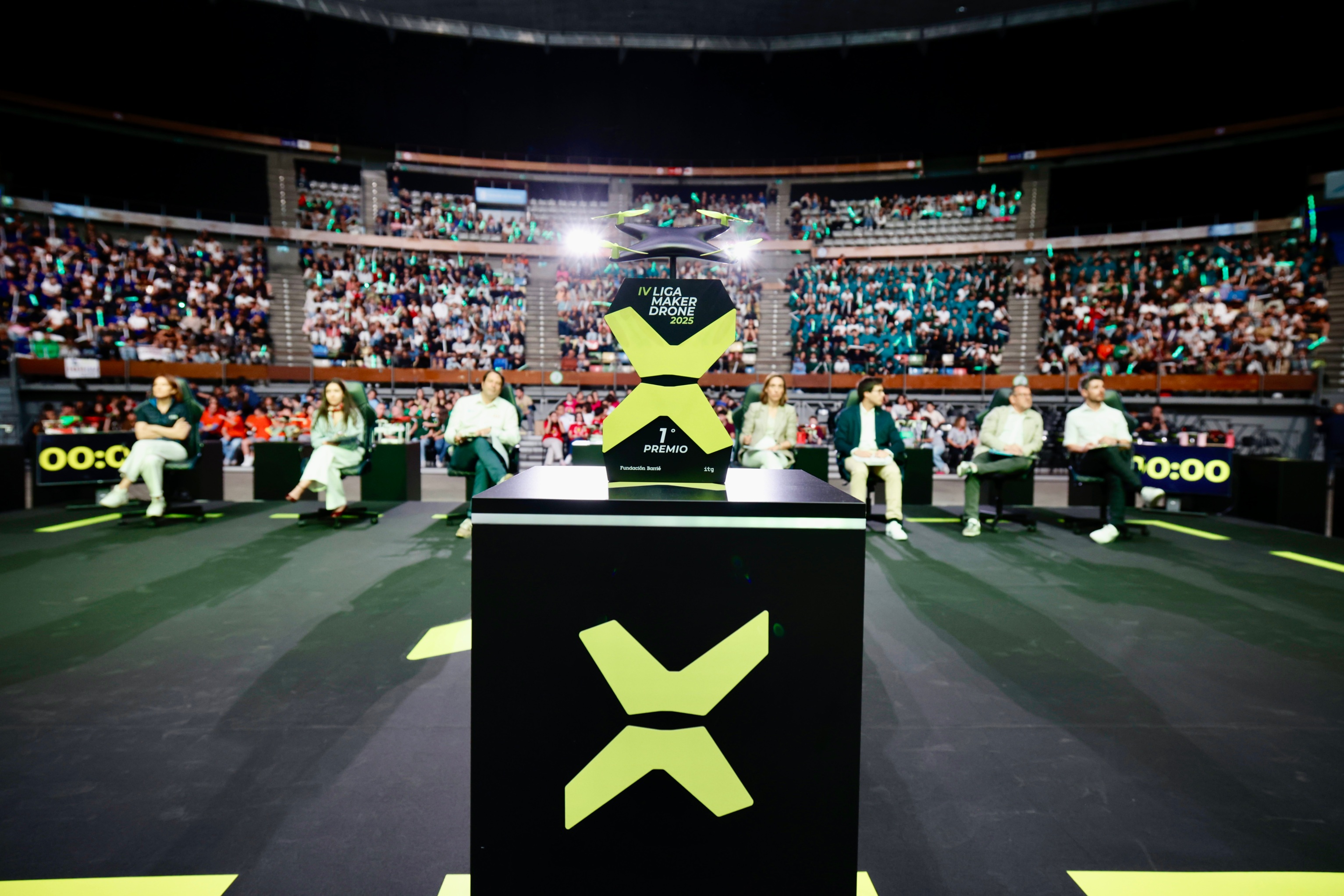 El trofeo de la IV Liga Maker Drone en primer plano y el jurado de esta edición. 